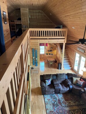 Interior de una cabaña de madera con habitación superior, comedor y sala de estar con sofá y alfombra.