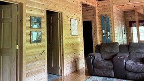 A log cabin interior with a balcony, wooden walls, a ceiling fan, and a patterned rug.