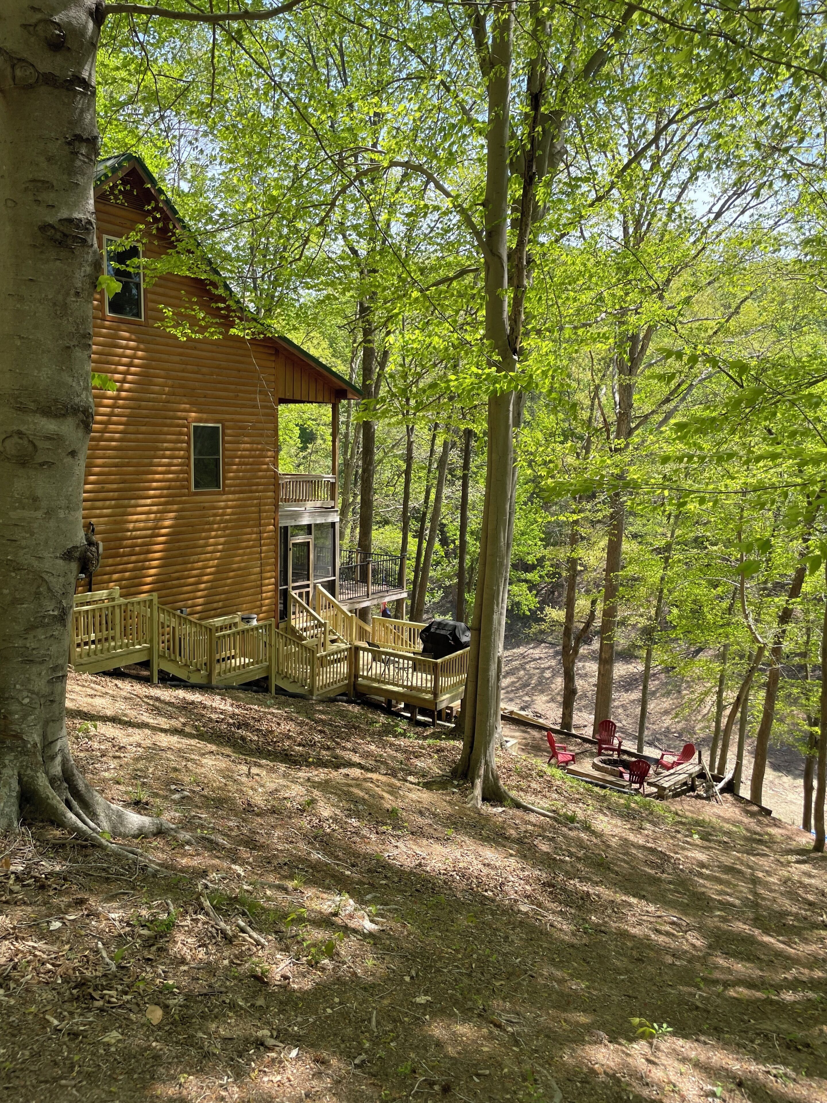 A wooden cabin with a deck and outdoor seating area surrounded by trees.