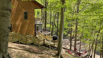 A wooden cabin with a deck and outdoor seating area surrounded by trees.