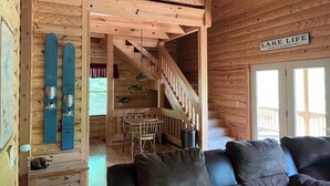 A wooden cabin interior with a dining area, a staircase, and a sign indicating it's unsalted & shark-free.
