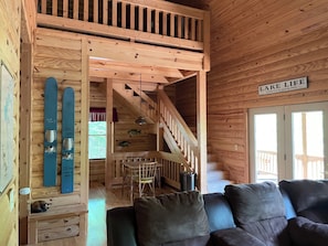 L’intérieur d’un chalet en bois comprend un coin repas, un escalier et une pancarte sur laquelle on peut lire : « LA VIE AU BORD DU LAC, SANS SELS NI REQUIN. »