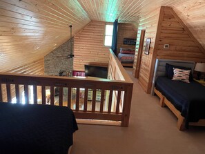 En hyggelig hytte med soveværelse i loftet, en stenspir og træloft.