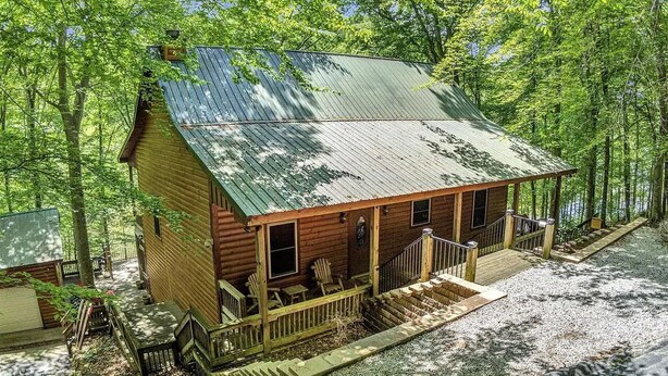 A wooden cabin with a porch, a small staircase, and a gravel driveway.