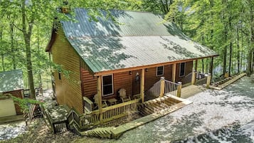 A wooden cabin with a porch, a small staircase, and a gravel driveway.