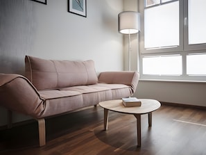 En moderne stue med en sofa, et rundt træbord, en gulvlampe og et stort vindue.