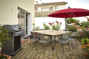 Un patio con una parrilla, mesa, sillas y un paraguas rojo.