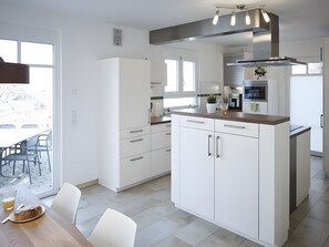 Et moderne køkken med hvide skabe, en indbygget ovn og et spiseområde med et bord og stole.