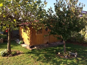 Una cabaña de madera con un porche pequeño, rodeada de un césped y árboles.
