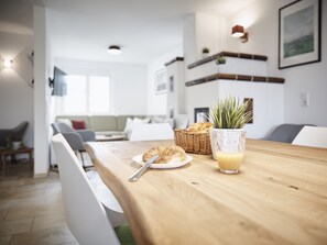 Una cocina moderna con una mesa de madera, una cesta de pan, un vaso de zumo de naranja y una silla blanca.