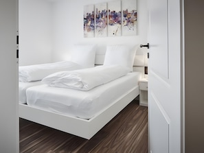 Un dormitorio moderno con una cama blanca, una mesita de noche y una obra de arte colgada en la pared.