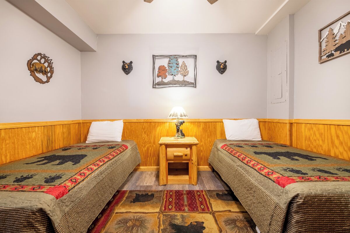 A room with two beds, a small wooden nightstand with a lamp, and decorative wall art.