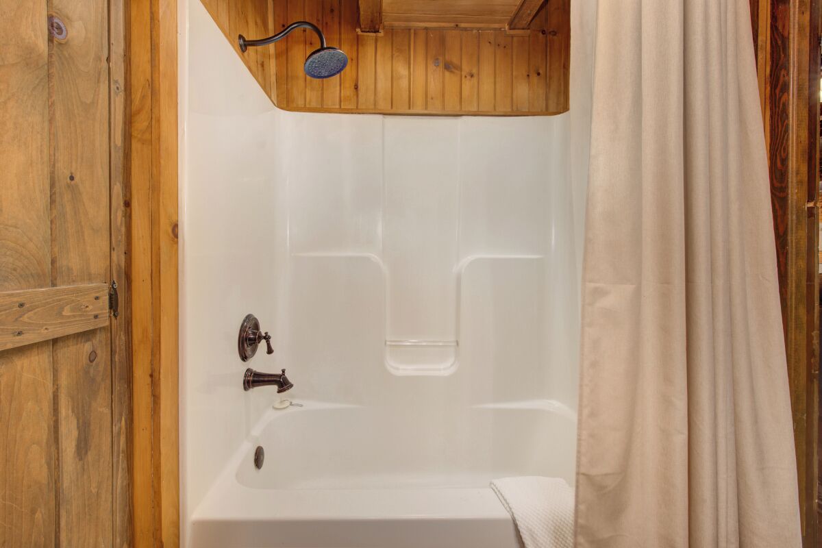 Une salle de bain aux murs lambrissés, avec une baignoire blanche et un rideau de douche.
