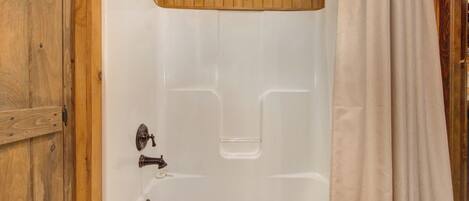 Une salle de bain aux murs lambrissés, avec une baignoire blanche et un rideau de douche.