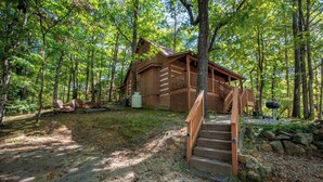 Una cabaña rústica con una terraza de madera y una escalera que lleva a la entrada.