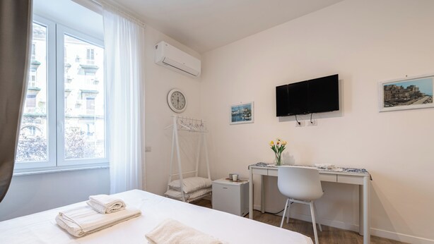 A hotel room with a bed, a desk, a chair, a TV, and a window with curtains.
