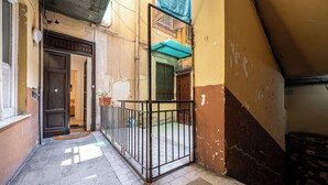 A narrow alleyway with a metal gate, a tiled floor, and a building with a green awning.