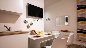 A compact kitchen with a sink, a flat-screen TV, and a small dining area with chairs and a table set for two.