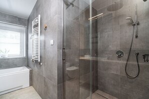 A modern bathroom with a glass-enclosed shower, a white bathtub, and a glass door. - RentPlanet - Apartament przy Plantach (Kraków)