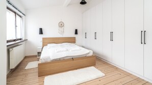 A modern bedroom with a wooden bed, white walls, and a large wardrobe. - RentPlanet - Apartament przy Plantach (Kraków)