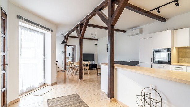 A modern kitchen with wooden beams, a dining area with chairs, and a large window. - RentPlanet - Apartament przy Plantach (Kraków)