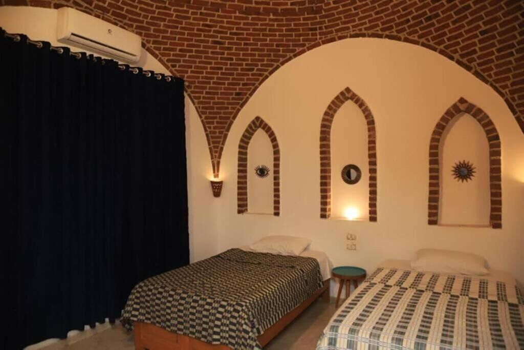 A room with two beds, a brick ceiling, and decorative wall sconces.