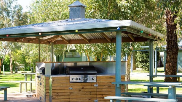 A wooden barbecue area with a metal grill, benches, and a covered shelter. - Kalganyi Holiday Park (Mount Gambier)