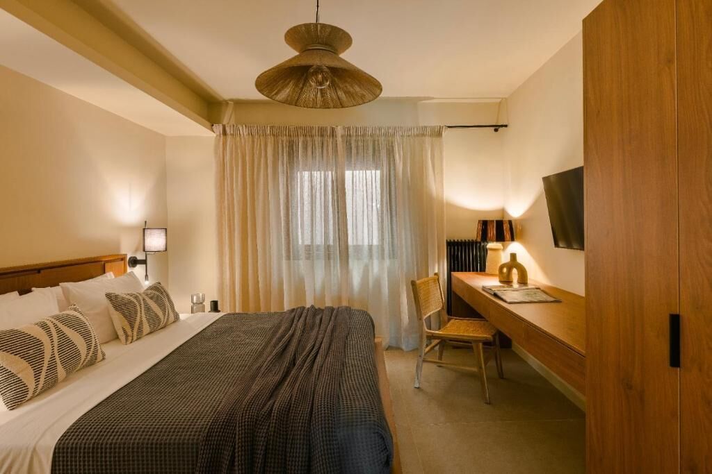 A hotel room with a bed, a desk, a chair, a television, and a window with curtains.