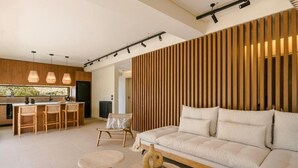 A modern living room with a sofa, a round table, and a chair. There is a kitchen area with a dining table and chairs. - The Attican Villa & Estate (Saronikos)