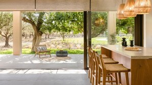 A modern kitchen with a large island, bar stools, and a view of a landscaped garden. - The Attican Villa & Estate (Saronikos)