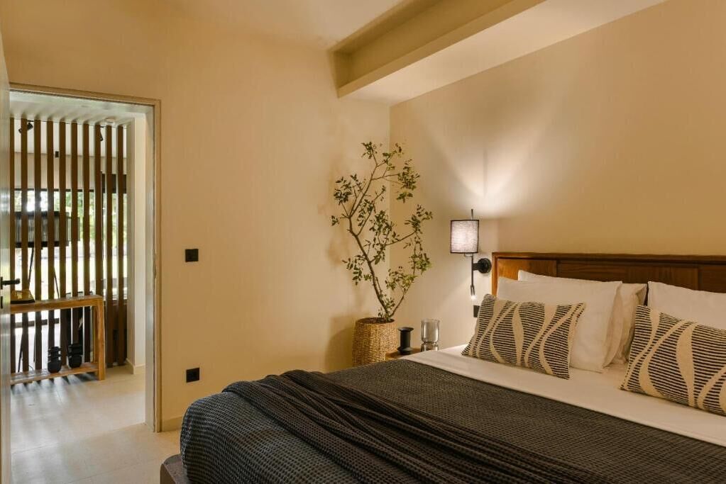 A bedroom with a bed, bedside table, lamp, and a potted plant.