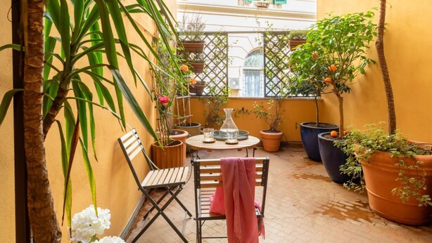 A small outdoor patio with a wooden table, chairs, and potted plants.