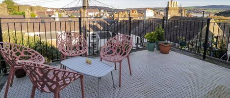 En balkon med et bord og stole, plantekasser og udsigt over bybilledet.