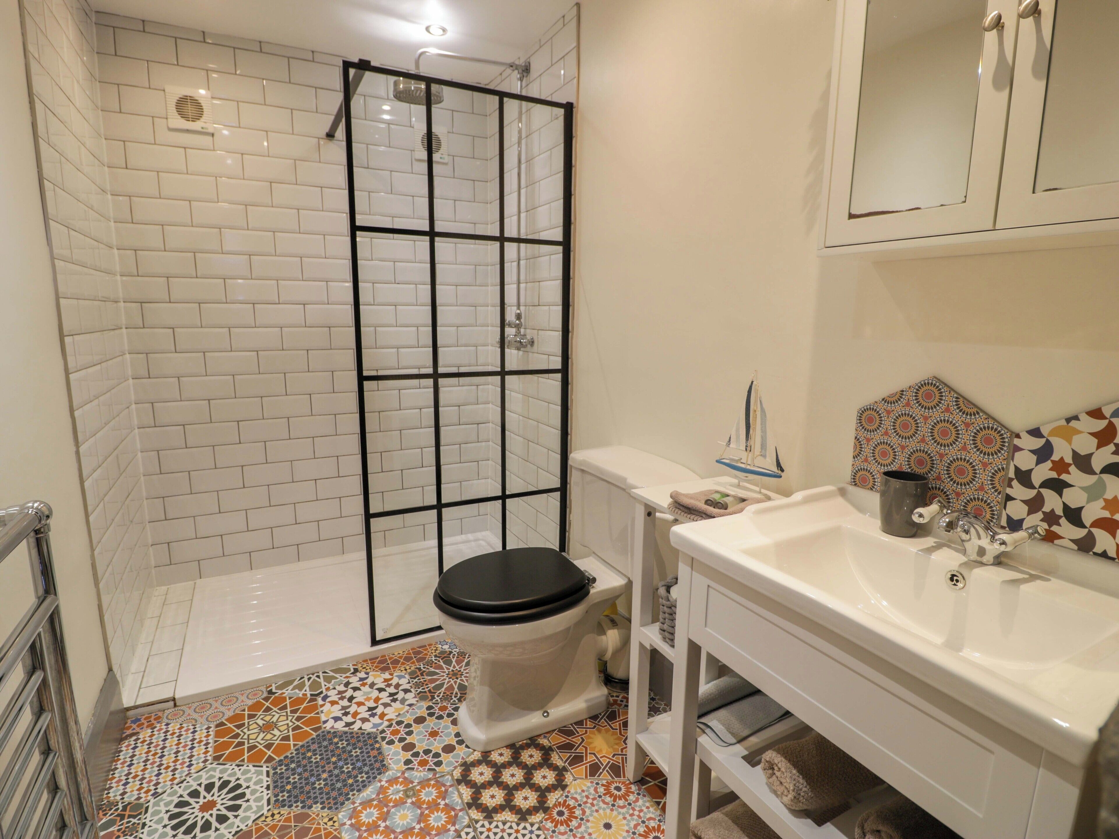A bathroom with a shower enclosure, a toilet, a sink, and a patterned floor.