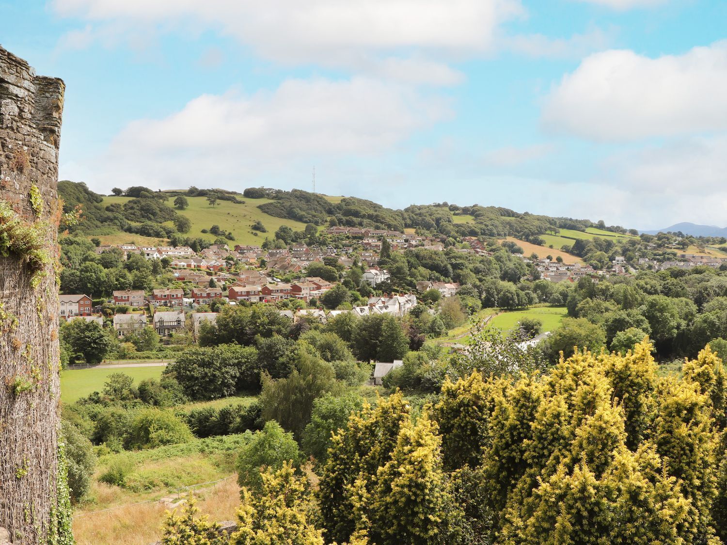 A rural landscape with a historic stone tower, rolling hills, and a small village with houses.