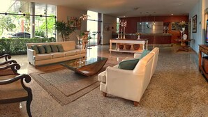 Amplia sala de estar con sofá, sillones y una mesa de centro. Se observa una cocina al fondo, con una barra y una mesa de comedor.