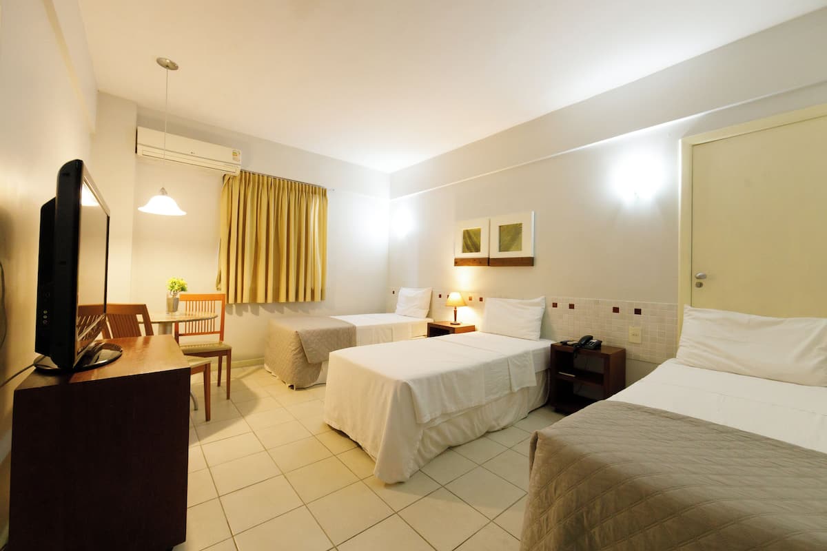 Une chambre d’hôtel avec deux lits, un bureau avec un ordinateur, une chaise, une petite table avec une plante et une fenêtre avec des rideaux.