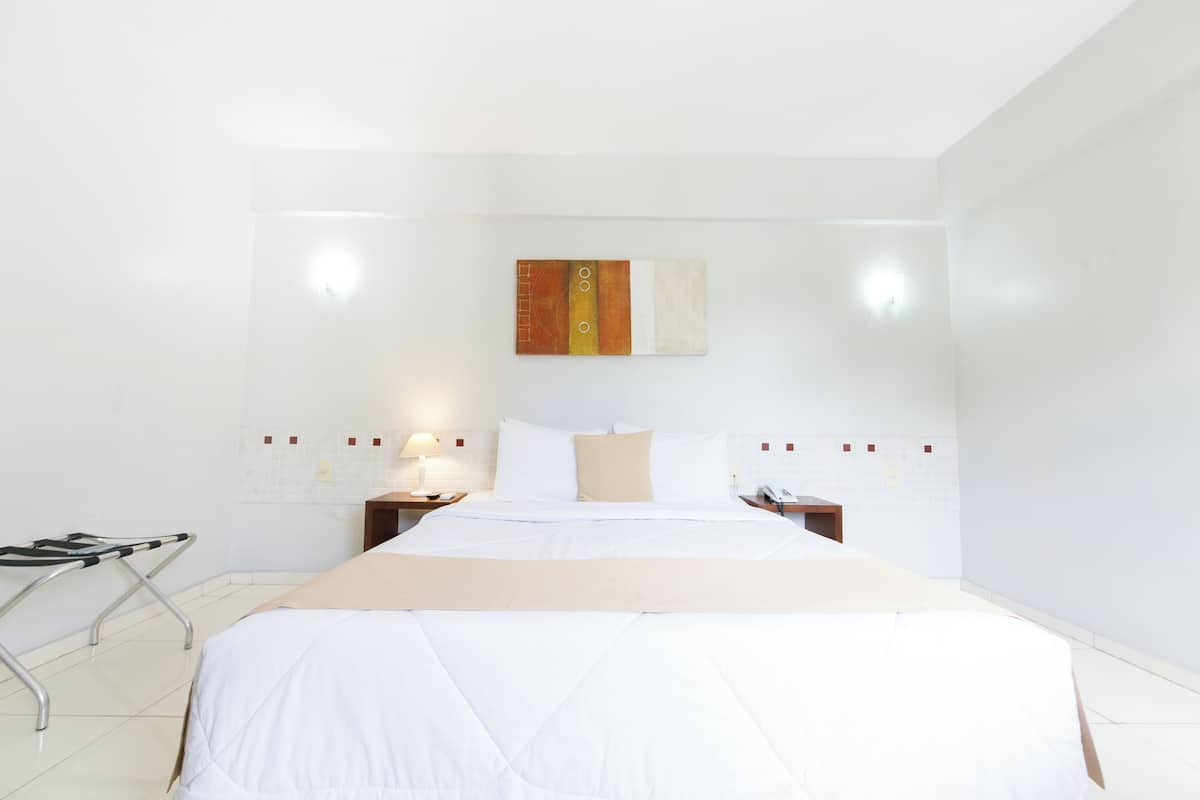 Une chambre d’hôtel comprenant un lit, des tables de chevet, une lampe et une œuvre d’art accrochée au mur.
