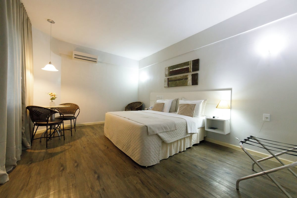 Une chambre à coucher comprenant un lit, une table de chevet, une lampe, une chaise et un étendoir.