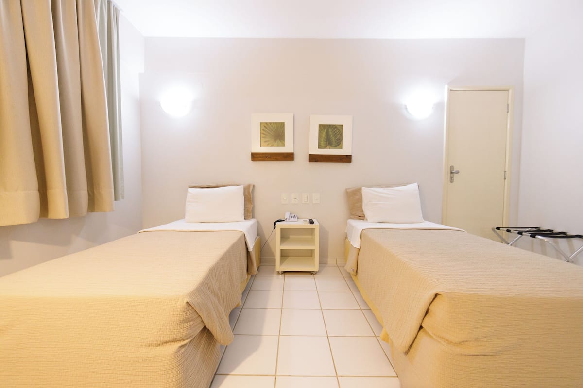 Une chambre d’hôtel avec deux lits simples, une table de chevet avec une lampe et une porte.