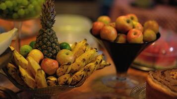 Un frutero con plátanos, manzanas y una piña sobre una mesa de madera.