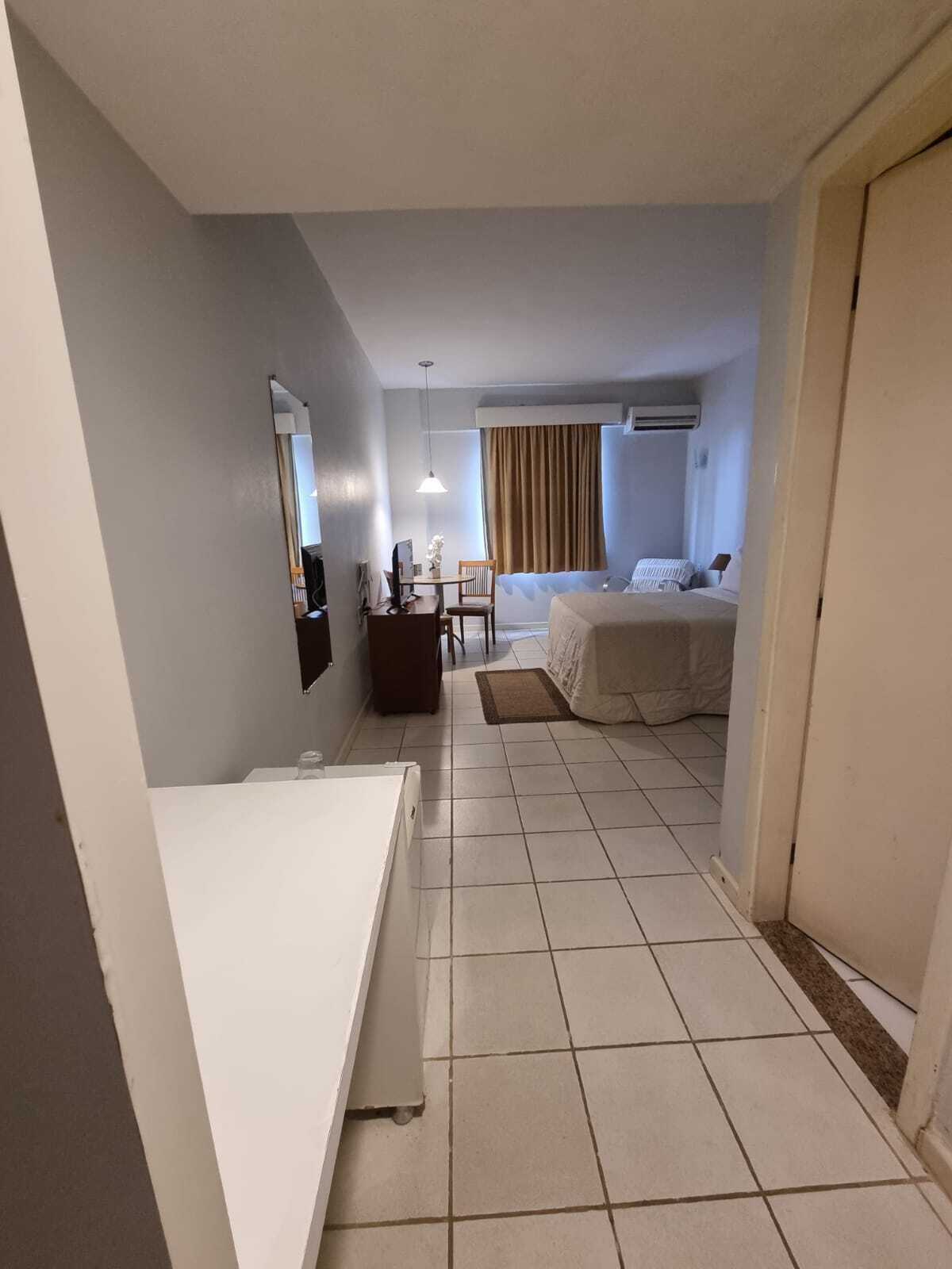 A hotel room with a bed, a desk with a chair, a small table, a mirror, and a window with curtains.