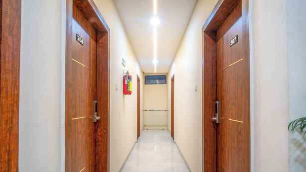 Un pasillo con puertas de madera, números 204 y 207, un extintor y una ventana al final.
