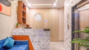 Una zona de recepción con mostrador de mármol, un reloj, un letrero de recepción y un ascensor.