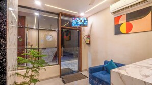 Una moderna zona de recepción con un mostrador de mármol, un sofá azul, una planta en maceta, una puerta de cristal que da a un pasillo y un televisor montado en la pared.