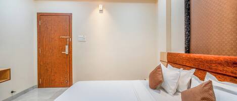 A bedroom with a wooden door, a bed with white bedding and brown pillows, and a headboard with a textured pattern.