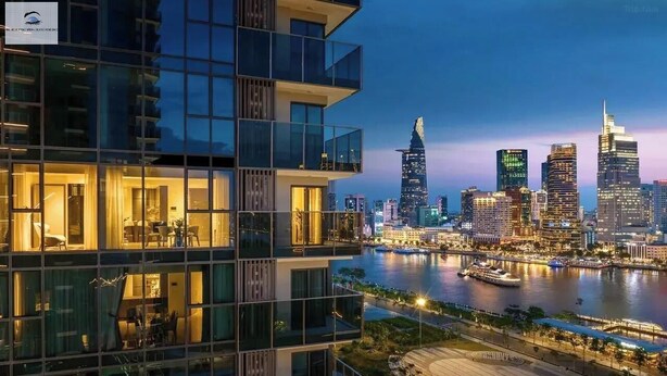 Un hotel moderno con varios pisos, ventanas amplias y vistas a un horizonte urbano y un río al atardecer.