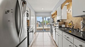 A modern kitchen with stainless steel appliances, a large island with bar stools, and a view to the outside. - Spacious Preston Hollow Condo (Dallas)