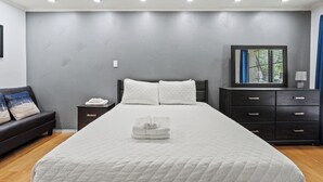 A modern bedroom with a large bed, a nightstand, a dresser, and a window with blinds. - Spacious Preston Hollow Condo (Dallas)