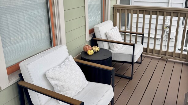 A covered porch with two white cushioned chairs and a small round table, featuring a view of a house with green siding and a white roof. - Bright & Airy 2-bed, 2.5-bath house in historic Germantown, Nashville (Nashville)